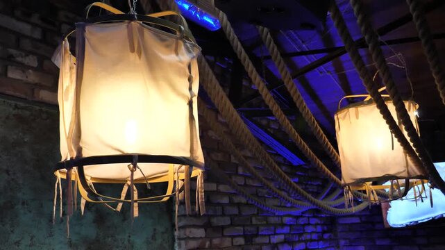 Cozy interior view of unique vintage pendant ceiling lamps with white fabric shades and thick decorative ropes in a dimly lit bar