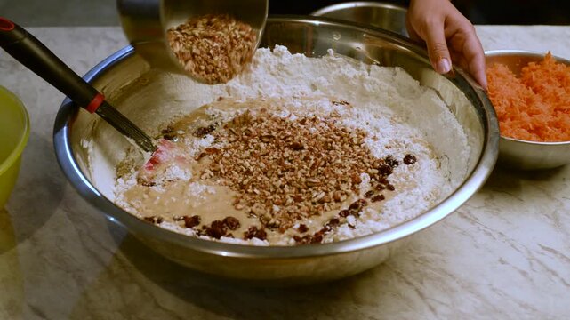 Female Hands Adding Nuts to Cake Batter in a Metal Bowl