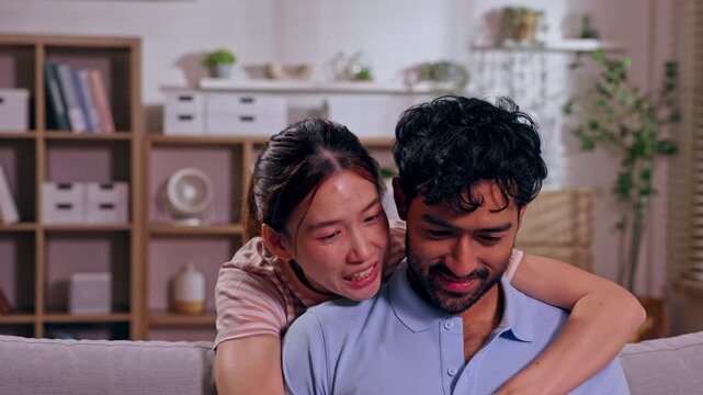 Asian couple young adult woman embracing man, emotional affection, relationship, laughter and sadness expressed through intimate sofa embrace home, comfortable living room with bookshelf