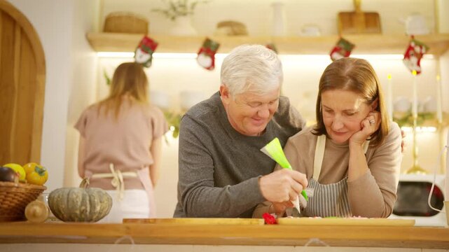 Happy family Christmas festive holiday celebration. Senior parents and adult daughter preparing and decorating holiday cookies together. Caucasian family enjoy festive treats in the kitchen.