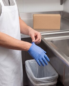 Food handler removing disposable glove beside waste bin