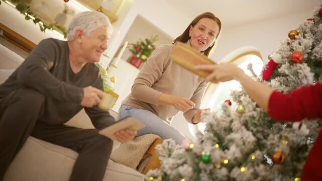 Happy family Christmas festive holiday celebration. Senior parents and adult daughter decorating Christmas tree together in living room. Happy Caucasian family enjoying tradition seasonal celebrating