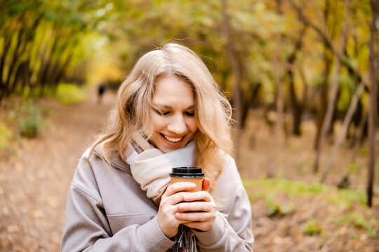 Smiling woman with cup in autumn outdoor &mdash; joy in true solitude. Peaceful lady drinking coffee in fall park surrounded by golden leaves. Slow living and resting from modern daily routines.