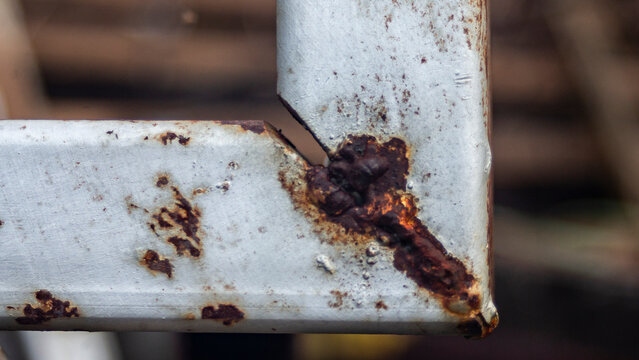 Close up of severe rust corrosion on an iron frame corner weld joint.A high-quality close-up macro shot focusing on severe rust corrosion at the welded corner joint of a hollow square iron frame. 
