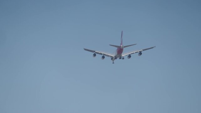 Low angle view of Qantas passenger airplane flying with landing gear extended against clear blue sky