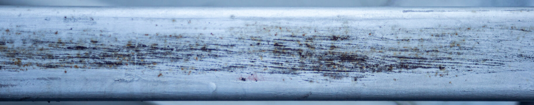 Horizontal close up of heavily scratched rusty metal bar texture.A high-resolution, panoramic-style close-up shot focusing on a weathered horizontal silver or grey painted metal bar. 