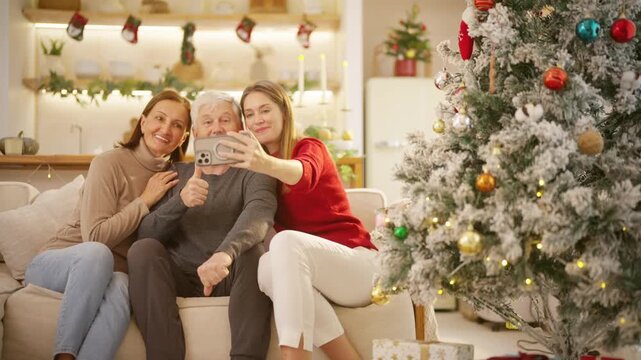 Happy Caucasian family enjoy Christmas holiday celebration at home. Senior parents and adult daughter using smartphone taking selfie together by decorated Christmas tree in living room.