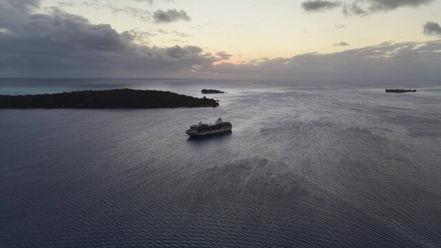 Aerial drone shot moving forward from a distance and panning down over calm twilight waters, revealing an anchored cruise ship and Motu Toopua in Bora Bora
