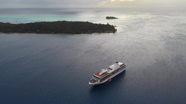 Aerial drone shot moving forward from a distance and panning down over calm twilight waters, revealing an anchored cruise ship and Motu Toopua in Bora Bora