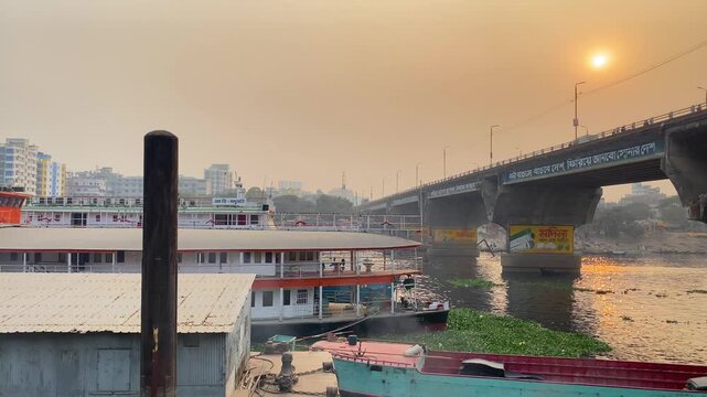 Common Myna Birds Flying Over A Rocket Paddle Steamer Boat On The Polluted Buriganga River At Sunset In Dhaka, Bangladesh. - wide shot