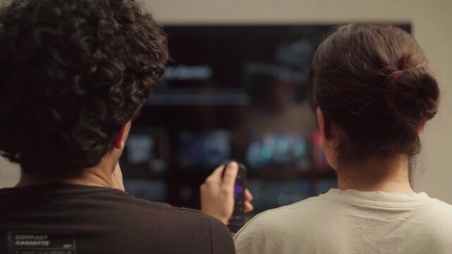 Couple watching streaming service menu on TV with remote control before screen goes black, turning off 