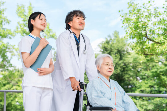 Doctor and Nurse Accompanying a Senior Patient in a Wheelchair Outdoors at a Hospital