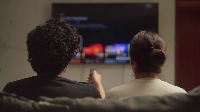 Relaxed couple choosing movie from streaming platform on smart TV for date night at home