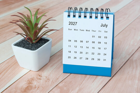 July 2027 desk calendar with potted plant on wooden desk.