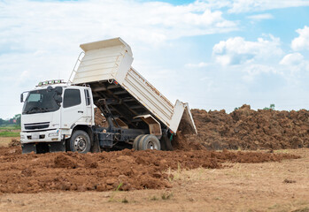 White dump truck unloading soil and dirt at an outdoor construction site or land development area. © Zblaster