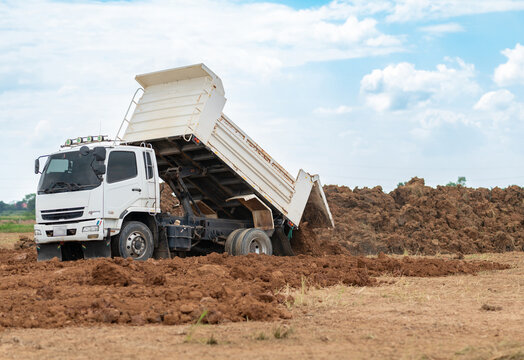 White dump truck unloading soil and dirt at an outdoor construction site or land development area.