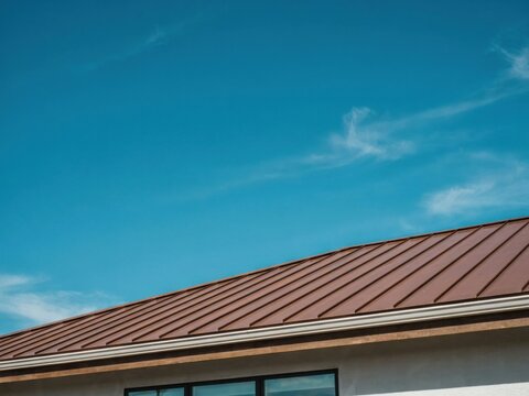Modern brown metal roof installed on residential house under clear blue sky offers durable and energy efficient protection.
