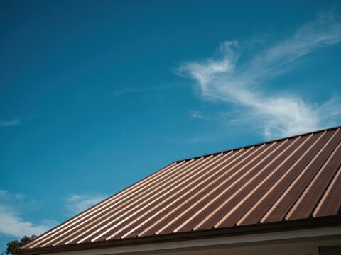 Standing seam brown metal roofing panels create clean geometric lines on modern house exterior against blue sky background.