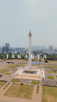 Vertical Aerial High-Angle Shot of the National Monument (Monas) in Central Jakarta with "JAKARTA" Text Overlay and City Skyline