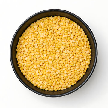 Top-down macro shot of dense yellow moong dal split pulses served in a simple black bowl isolated on a clean white background