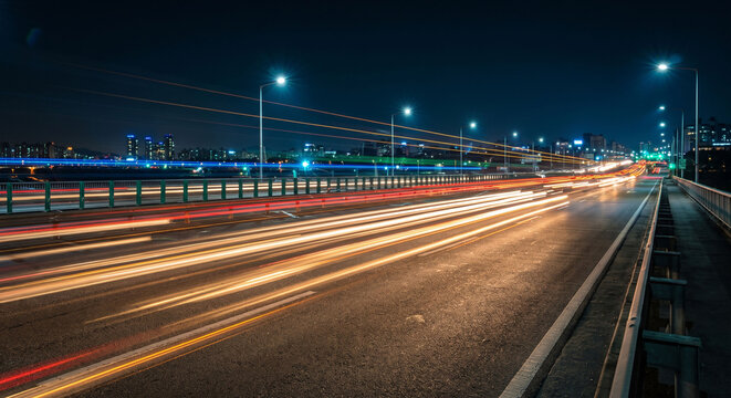 Long exposure light trails of traffic on a curved highway leading to the city skyline at night, Night traffic on a busy freeway with red and white blurred light streaks and cityscape.