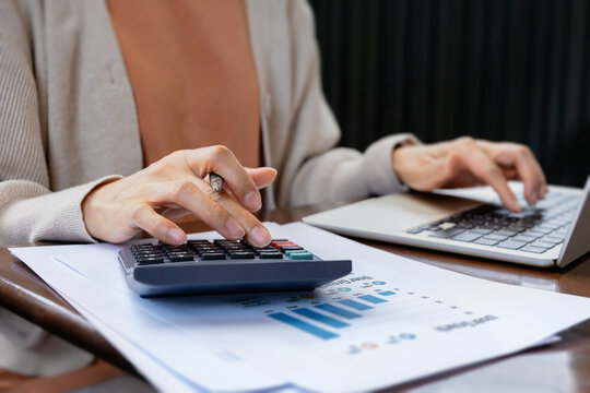 Woman hands using calculator and typing on laptop computer with financial report paperwork on table. Accounting concept