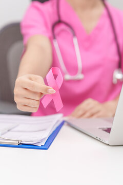 Doctor wearing lab coat giving pink ribbon to patient for Breast Cancer Awareness month, World Cancer Day, National Cancer Survivors Month, Pink October and Women Health empathy concept 
