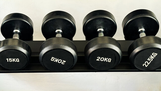 Black dumbbells of different weights arranged on a storage rack in a modern gym. Strength training and fitness equipment for weightlifting, functional workouts and exercise.