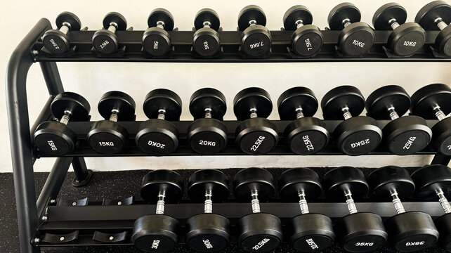Black dumbbells of different weights arranged on a storage rack in a modern gym. Strength training and fitness equipment for weightlifting, functional workouts and exercise.