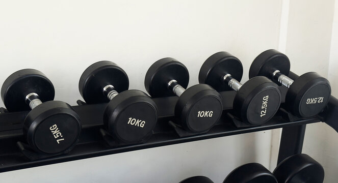 Black dumbbells of different weights arranged on a storage rack in a modern gym. Strength training and fitness equipment for weightlifting, functional workouts and exercise.