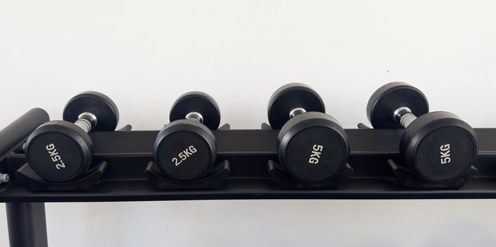 Black dumbbells of different weights arranged on a storage rack in a modern gym. Strength training and fitness equipment for weightlifting, functional workouts and exercise.