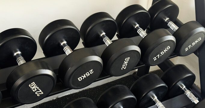 Black dumbbells of different weights arranged on a storage rack in a modern gym. Strength training and fitness equipment for weightlifting, functional workouts and exercise.