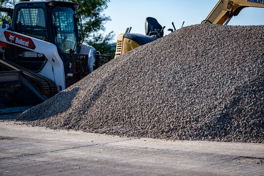 Wisconsin, USA - Jul 12, 2026: Stockpile of gray crushed stone or construction aggregate with Bobcat skid-steer loader heavy machinery along a roadside. Editorial Use Only.