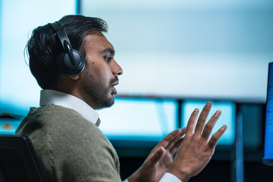 A male support consultant gesturing while working through a ticket presses his hands together as he apologises for a service delay at a busy technology workplace