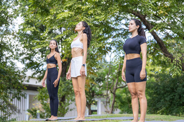 Fototapeta premium A group of three Hispanic women in sportswear, talking as they walk, carry their mats along a shaded walkway one fixing her hair as they walk, an image about women and fitness.