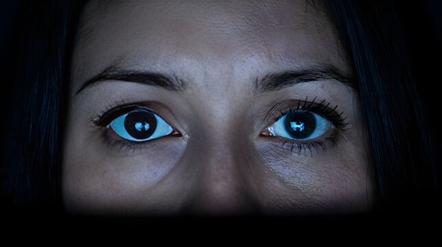 Close up of young woman face with screen reflection in eyes in dark