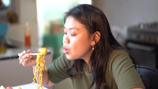 Asian woman eating noodles with chopsticks at home in the kitchen