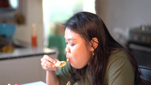 Young Asian woman eating spring roll at home