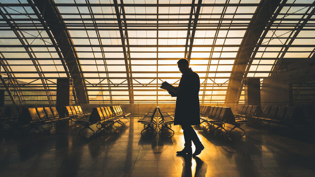 Man walks and reads a book in airport terminal at sunrise