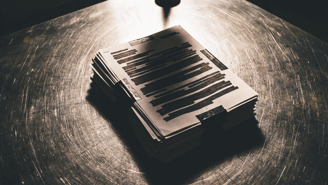 Heavily redacted stack of confidential papers on metal surface