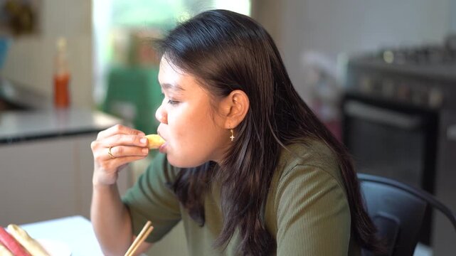 Young Asian woman eating spring roll with chopsticks at home