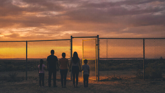 Parents and children stand holding hands at an open desert gate at dusk