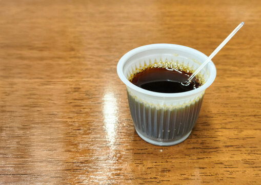  Plastic cup of black coffee with stirrer on wooden table