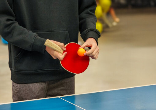  Person holding table tennis paddle and ball beside blue ping pong table
