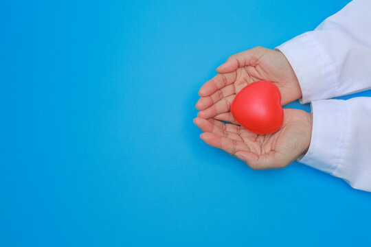 Compassionate doctor hand holding red heart symbol promotes health awareness and reduces risk with gentle medical care support on blue background