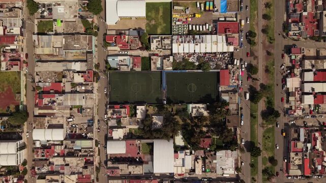 Smooth top down drone descent over soccer fields in Ecatepec, Mexico, with people playing, surrounding houses, cars and residential streets