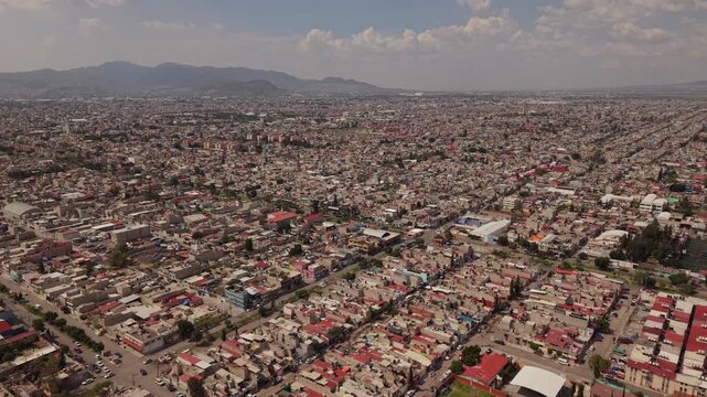 Aerial drone view over residential neighborhoods in Ecatepec, Mexico, with houses, people, cars, mountains and clouds under sunny skies