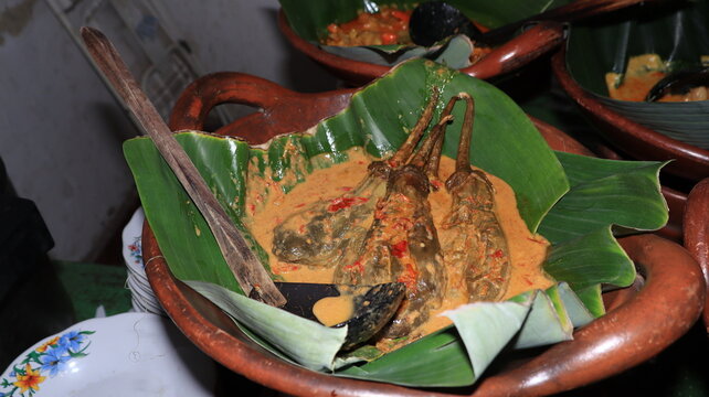 Spicy indonesian eggplant dish beautifully presented in a rustic clay pottery bowl lined with vibrant green banana leaf for authentic heritage diner setup.