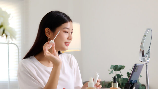 Close-up of a young Asian woman applying eyeshadow with a small makeup brush in front of a mirror, ideal for cosmetics, beauty tutorials, and skincare content.