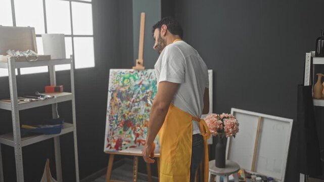 Man painter in yellow apron holds brushes in right hand and smiles while posing in studio; creative joy.